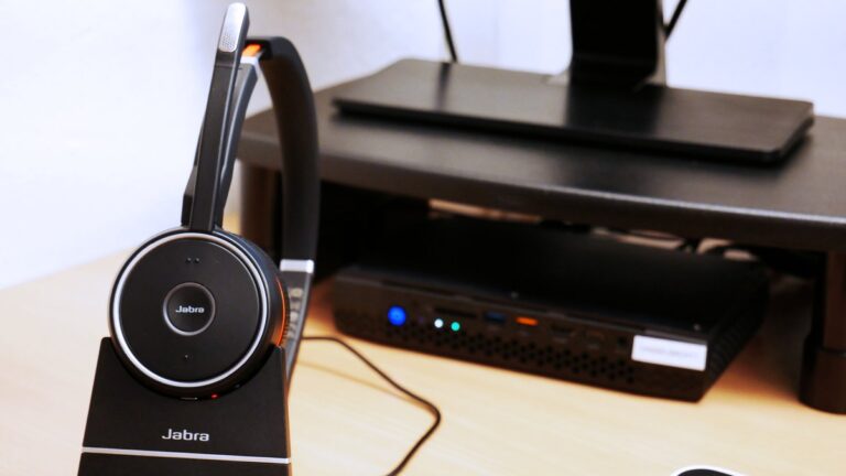 VoIP-Headset in der Ladestation neben einem Mini-PC am Schreibtisch